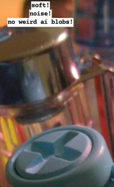 Zoomed in to just the ends of 2 pens, one blue with a cross and the other metallic, from the first image.
Text annotation towards top left: soft!
noise!
no weird ai blobs!