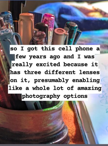 Close up photograph of a clay pen holder full of pens on a desk next to the edge of a notebook. Center text annotation: so I got this cell phone a few years ago and I was really excited because it has three different lenses on it, presumably enabling like a whole lot of amazing photography options.
